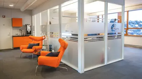Kontorlandskap med oransje stoler og foliert glassvegg hos Braathe Gruppen.