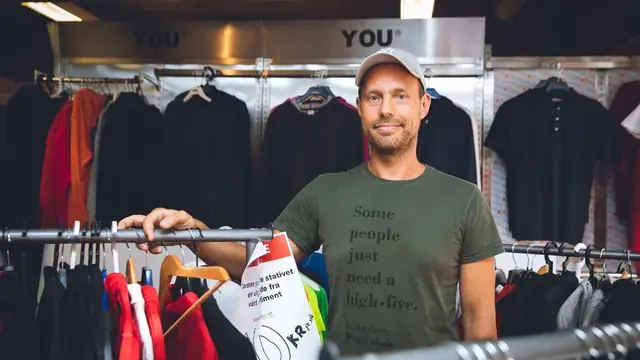 Mann i grønn t-skjorte ved stativer fulle av profilplagg i butikken hos Kopisenteret.